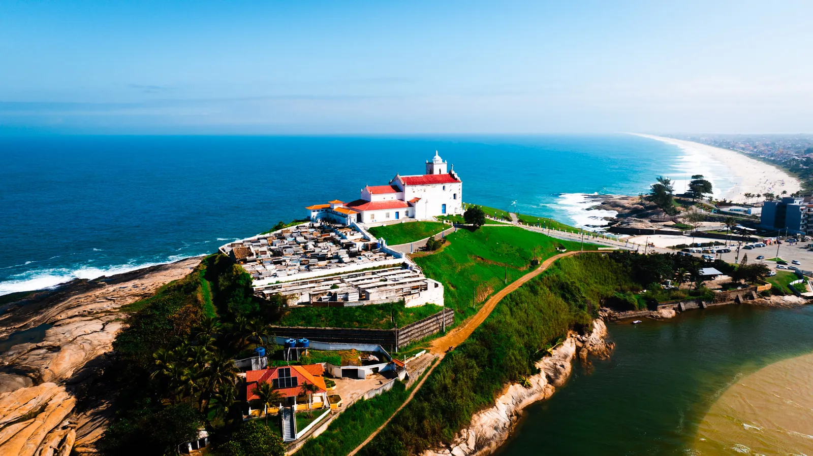 Igreja histórica sobre promontório entre o mar e a lagoa, vista aérea