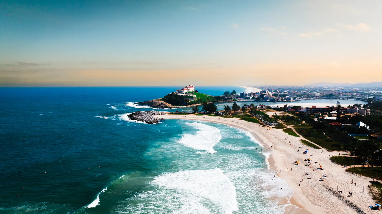 Vista aérea de praia com igreja histórica sobre o morro e mar azul